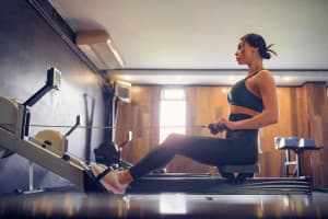 Determined young woman working out on row machine in fitness studio